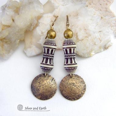 Bold and unique, these handcrafted earrings have an ethnic African tribal vibe. They feature gold brass dangles with a hammered rustic texture accented with exotic African beads with an intricate brown and white carved pattern topped off with gold brass beads. Unique and fun to wear - they'll make a bold, striking statement. Perfect for women that love to wear one-of-a-kind artisan handcrafted jewelry. Handmade in the USA by Silver and Earth Jewelry. 