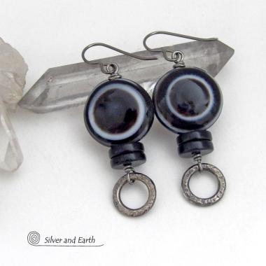 These earrings feature big natural black eye agate stones accented with black onyx and small hammered silver pewter circle dangles. When cut at the right angle, this type of agate reveals a series of concentric rings that resembles the human eye. They have a funky, modern vibe and are unique and fun to wear. They'll make a bold statement and are perfect for women that love to wear unique natural stone jewelry. 