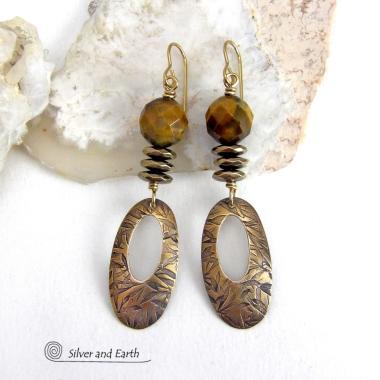 These handcrafted earrings feature gold brass oval hoop dangles with a hand stamped texture accented with natural brown tiger's eye gemstones and faceted hematite stones with an electroplated champagne gold finish. The stones have a beautiful brown hue with undertones of gold and a faceted finish which casts off a natural sparkle and shine. They have a modern, chic and elegant style that coordinates beautifully with all wardrobe types - dressed up or down.